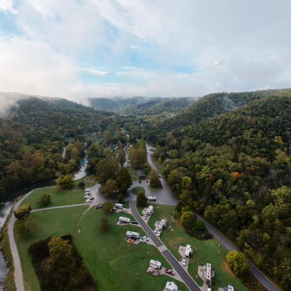 Aerial drone photograph of fog rising over the Ozark hills in Missouri after a rainstorm, showing trees, rolling landscape, and a campsite captured by Reel Drone Rangers.